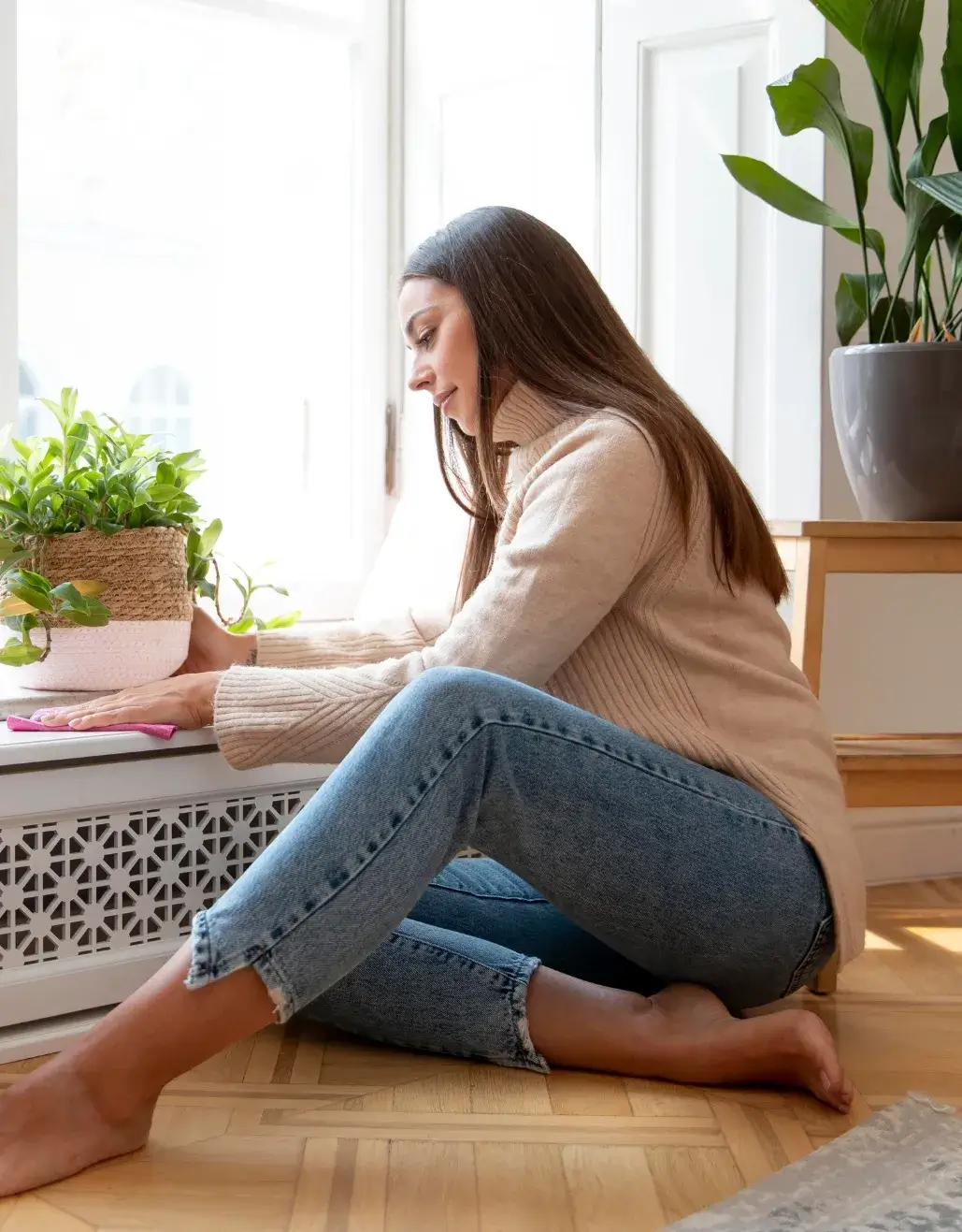 Woman wiping a windowsill during spring cleaning with a potted plant nearby.